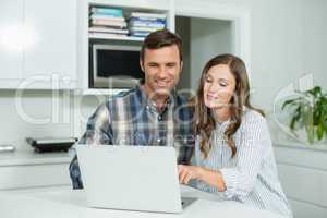Happy couple interacting with each other while using laptop in living room