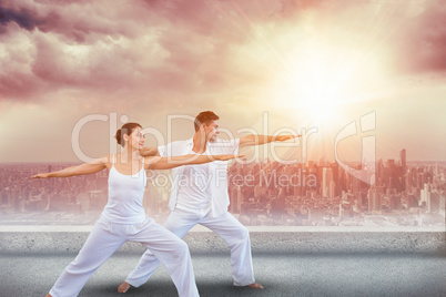 Composite image of peaceful couple in white doing yoga together in warrior position
