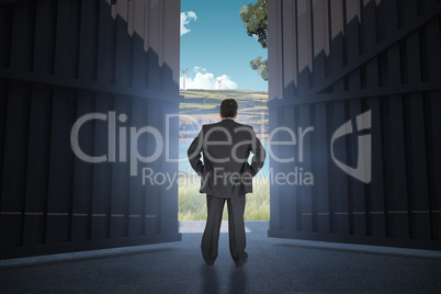 Composite image of businessman standing back to the camera with hands on hip  3d