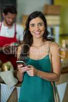 Portrait of smiling woman using mobile phone at counter