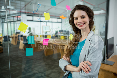 Smiling female executive standing with arms crossed in creative office