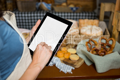 Mid-section of staff using digital tablet at bakery counter