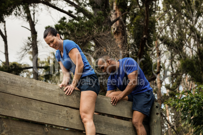 Male trainer assisting woman to climb a wooden wall