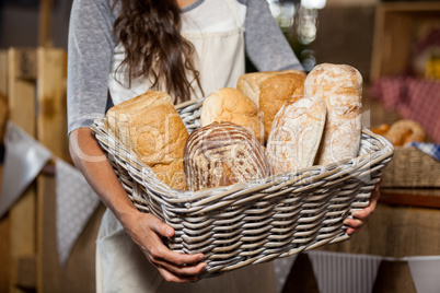 Female staff holding wicker basket of various breads at counter in bakery shop