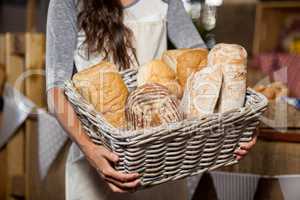 Female staff holding wicker basket of various breads at counter in bakery shop