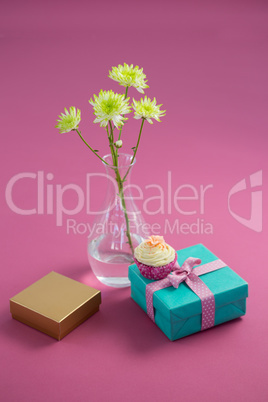 Flower vase and cupcake with gift boxes against pink background