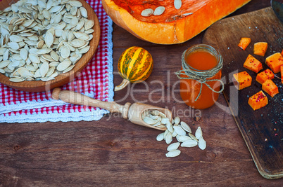 Pumpkin seeds and a piece of fresh pumpkin on a brown wooden sur