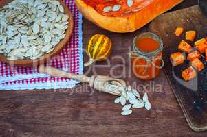 Pumpkin seeds and a piece of fresh pumpkin on a brown wooden sur