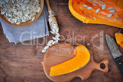 Piece of fresh pumpkin and pumpkin seeds on a brown table