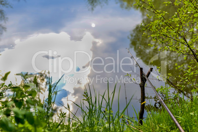 Fishing rod on the river bank among greenery on a fishing trip in the spring