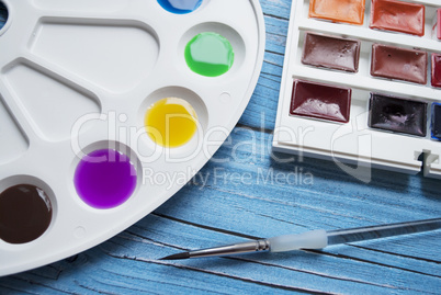 Artist workspace composition with brush, palette and watercolor on a blue wooden background.