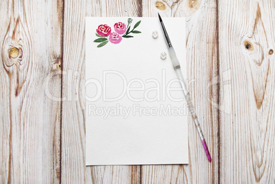 Blank paper with painted roses with the place for your text on a wooden background.
