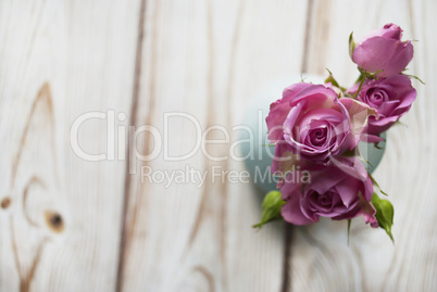 Vase with a bouquet of pink roses on a wooden background with the place for your text.