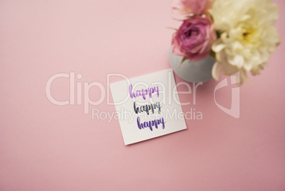 Happy written in calligraphy style on paper with bouquet of pink roses and white chrysanthemums on a pink background. Flat lay, top view
