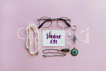 Shine on handwritten with watercolor in calligraphy style. Women's fashion accessories arrangement on a pink background. Flat l