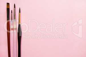 Paint brushes on a pink background with the place for your text. Top view