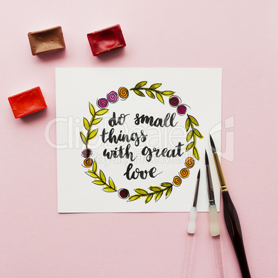 Inspirational quote do small things with great love , watercolor, brushes on a pink background. Artist workspace. Flat lay