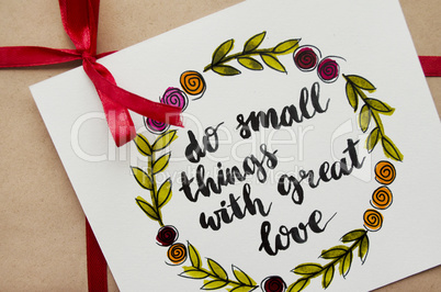 Inspirational quote do small things with great love written in calligraphy style. Gift in kraft paper with a red ribbon. Flat lay