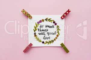 Inspirational quote do small things with great love handwritten with watercolor in calligraphy style, miniature clothespins on a pink background. Flat lay