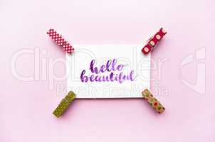 Inspirational quote Hello beautiful handwritten with watercolor in calligraphy style, miniature clothespins on a pink background. Flat lay