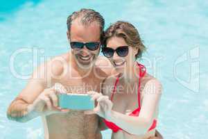 Happy couple taking selfie from mobile phone in pool