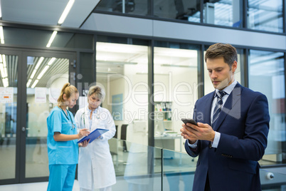 Businessman using mobile while doctor and nurse discussing over clipboard in background