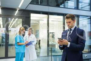 Businessman using mobile while doctor and nurse discussing over clipboard in background