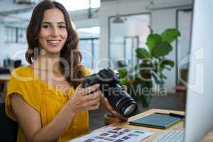 Smiling graphic designer holding digital camera in creative office