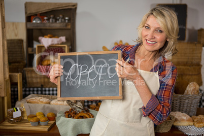 Portrait of smiling female staff holding chalkboard with open sign at counter