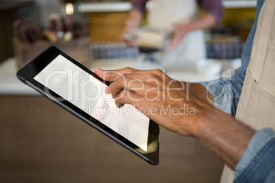 Mid section of male staff using digital tablet near meat counter