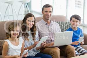 Smiling family using digital tablet, phone and laptop in living room at home