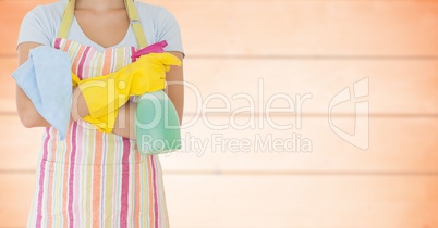 Woman in apron with arms folded and cleaner against blurry orange wood panel