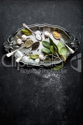 Dark culinary background with bay leaves, salt, pepper and garlic