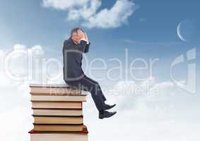 Businessman worried sitting on Books stacked by blue sky