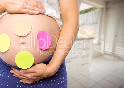 Pregnant woman mid section with sticky notes on stomach in blurry kitchen