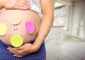 Pregnant woman mid section with sticky notes on stomach in blurry kitchen
