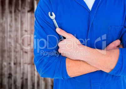 Mechanic arms folded with wrench against blurry wood wall
