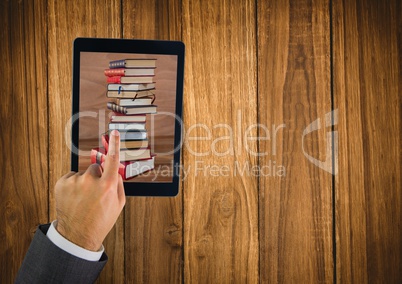 Hand touching tablet showing book pile on table