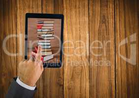 Hand touching tablet showing book pile on table