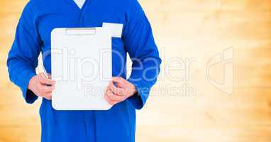 Mechanic holding up clipboard against blurry yellow wood panel