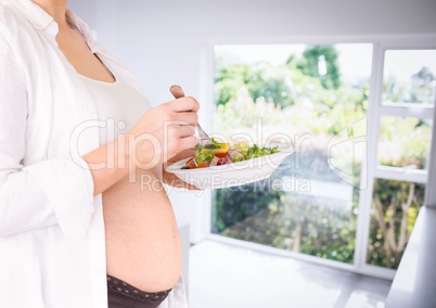 Pregnant woman mid section holding salad in blurry kitchen