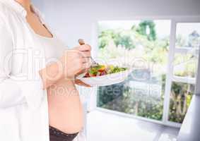 Pregnant woman mid section holding salad in blurry kitchen
