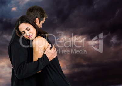 Sad couple hugging against dark cloudy sky