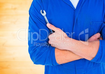 Mechanic arms folded with wrench against blurry yellow wood wall