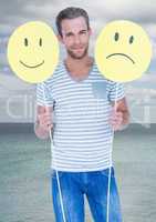Man holding happy and sad faces against sea