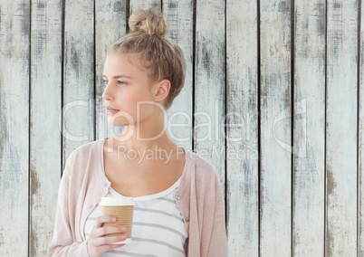 Woman looking to side holding coffee cup against wood panel