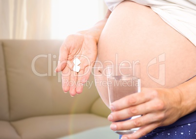 Pregnant woman mid section with medication in blurry sitting room