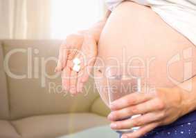 Pregnant woman mid section with medication in blurry sitting room