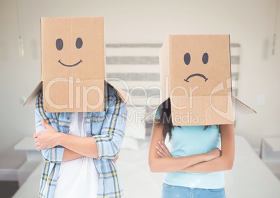 Couple with box heads sad and happy against bedroom