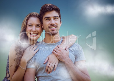 Woman with arms around man against blue green background with clouds